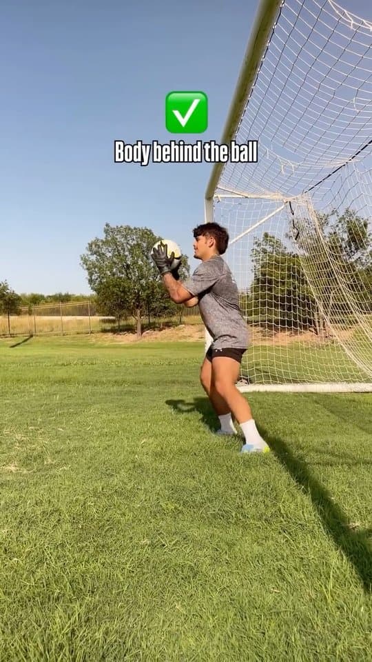 A young goalkeeper catching the ball with his body behind it